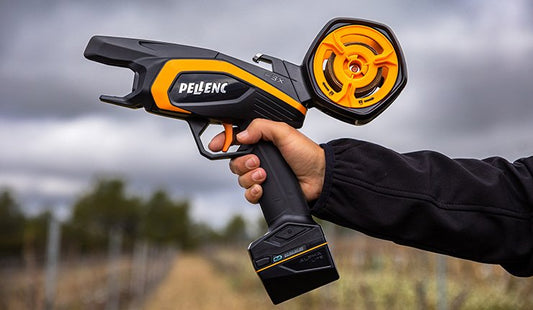 Worker holding an orange and black Pellenc F3X H35 battery-powered horizontal tying machine between vineyard rows
